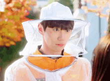 a young man wearing a beekeeper 's hat looks at a woman
