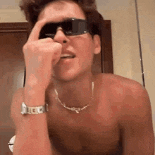 a shirtless man wearing sunglasses and a watch is making a face .