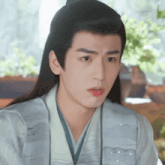 a young man with long hair is wearing a kimono and making a surprised face .