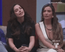 two women are sitting next to each other on a couch and talking to each other .