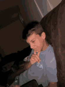 a young boy is sitting on a couch holding a remote control and wearing a t-shirt that says sca