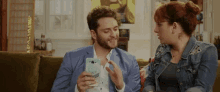 a man and a woman are sitting on a couch looking at a cell phone together .
