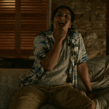 a woman in a hawaiian shirt is sitting on a bed