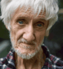 a man with white hair and a beard is wearing a plaid shirt and looking at the camera .