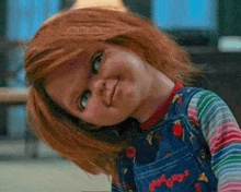 a close up of a doll with red hair and overalls making a funny face .
