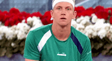 a man wearing a green shirt and a white headband is sitting in front of a bunch of flowers .