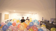 two men are standing in a room filled with lots of balloons