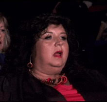 a woman in a red shirt is making a funny face while sitting in a theater .