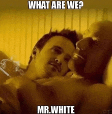 two men are laying on a bed and one is smoking a cigarette while the other looks on .