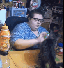a woman is playing with a cat next to a bottle of smuckers