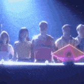 a group of people are standing around a table with a purple object on it