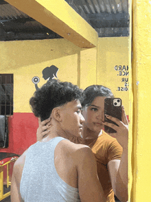 a man and a woman are taking a selfie in front of a yellow wall that says ' ice ' on it