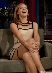 a woman in a dress is sitting on a couch laughing .