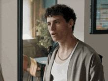 a man with curly hair and a white tank top is standing in a room .