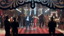 a man in a suit and a woman in a red dress are dancing on a stage .