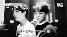 two young men are standing next to each other in a black and white photo with a mnet logo in the corner .