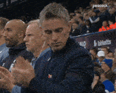 a man applauds in front of a peacock sign