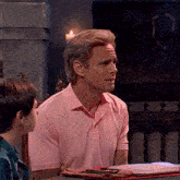 a man in a pink shirt sits at a table talking to a boy
