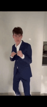 a young man in a blue suit and white shirt is standing in front of a white wall .