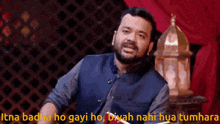 a man with a beard is sitting in front of a sign that says itna badha ho gayi ho byah nahi hua tumhara