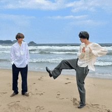 a man kicking another man on the beach with a blue sky in the background