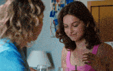 a woman in a pink tank top sits at a table with a glass of wine