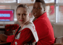 a girl in a red jacket with the letter o on it sits next to a boy in a red jacket