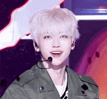 a young man with white hair is wearing a green jacket and a microphone on his neck .