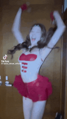 a woman in a red skirt is dancing in front of a door with her arms in the air .
