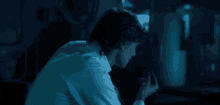 a man in a white shirt is sitting in the dark