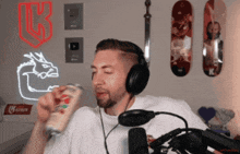 a man wearing headphones holds a can of soda in front of a neon sign that says k on it