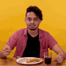 a man sitting at a table with a plate of food and a glass of cola