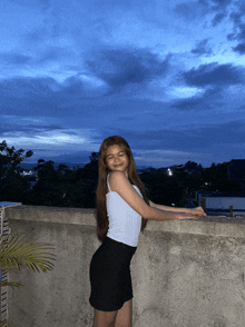 a woman in a white tank top and black skirt is standing on a ledge