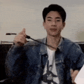 a young man in a denim jacket is holding a pen and making a funny face .