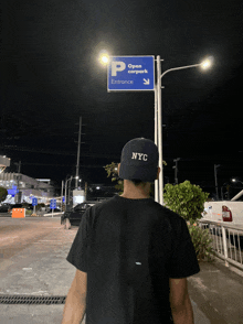 a man wearing a nyc hat is standing in front of an open carpark entrance sign
