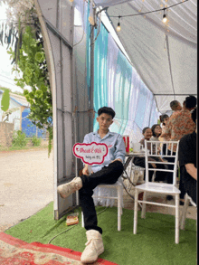 a man sits under a tent holding a sign that says " official rita "