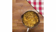 a pan of food is sitting on a wooden table next to a checkered table cloth .