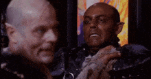 two men are standing next to each other in a dark room . one of the men has a beard .