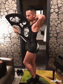 a man in a black bodysuit holds a fan with a dragon design on it