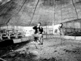 a black and white photo of a man sitting in a chair under a tent