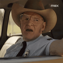 a man wearing a cowboy hat and glasses is sitting in a car with a max logo in the background