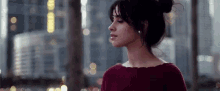 a woman in a red sweater and bun is standing in front of a city skyline .