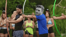 a man in a blue shirt is aiming a bow and arrow at another man