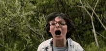 a young boy wearing glasses and a palm tree shirt is yawning in the woods