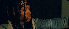 a man with dreadlocks wearing a bandana and a denim jacket is sitting in a car .