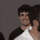a man in a white shirt is smiling while standing next to another man in a black shirt