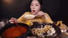 a woman in a yellow sweater is eating a spoonful of soup