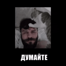 a man with a beard is laying down with a cat on his head .