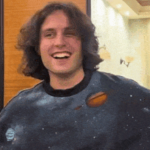 a man with long hair is wearing a sweatshirt with a planet on it .