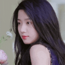 a close up of a woman 's face with purple hair and a flower in the background .
